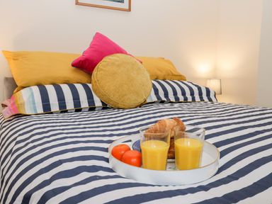 A bed with striped bedding pillows and a tray with orange juice croissants and oranges at Harbour Hideaway Whitby