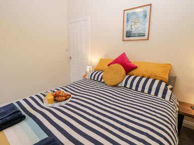 A bedroom with a striped bedspread croissants and orange juice on a tray and cushions on the bed at Harbour Hideaway in Whitby