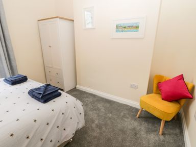 A bedroom with a bed with towels on it a wardrobe yellow chair with a red cushion and framed pictures on the wall at Harbour Hideaway in Whitby