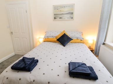 A bedroom with a bed with patterned bedding two bedside lamps and folded towels at Harbour Hideaway Whitby