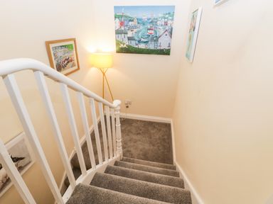 A staircase with grey carpet leading to a landing with a floor lamp and paintings on the walls at Harbour Hideaway in Whitby
