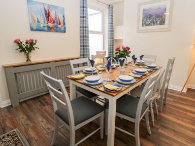 A dining room with a wooden table set for six people and chairs with cushions at Harbour Hideaway in Whitby