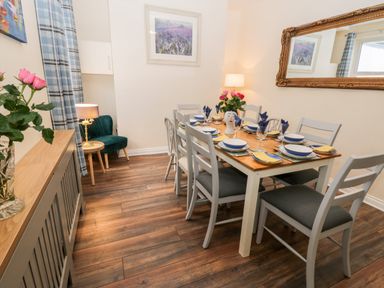A dining room with a wooden table set for eight people with plates glasses and napkins a sideboard with flowers a green chair a lamp a large mirror and a framed picture at Harbour Hideaway Whitby