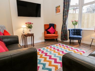 A living room with a wall-mounted TV colorful zigzag rug two armchairs and a sofa at Harbour Hideaway in Whitby