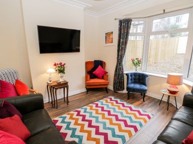 A living room with colorful chairs a zigzag patterned rug and a wall-mounted TV at Harbour Hideaway in Whitby