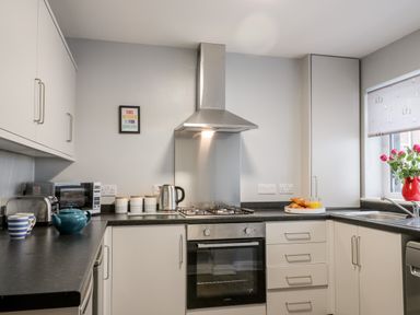 A kitchen with a gas stove oven range hood microwave toaster kettle cups a teapot and a window with flowers at Harbour Hideaway in Whitby