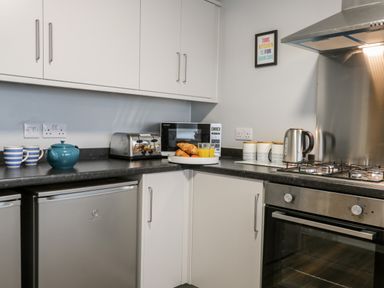 A kitchen corner with white cabinets a microwave toaster kettle oven and cups at Harbour Hideaway in Whitby