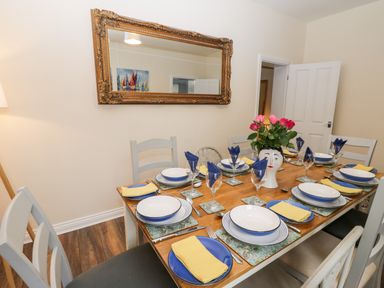 A dining table set with plates glasses and napkins with a vase of flowers and a large ornate mirror on the wall at Harbour Hideaway in Whitby