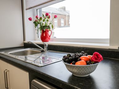 A kitchen sink with a bowl of fruit and a rose on the counter and a vase of roses on the windowsill at Harbour Hideaway in Whitby