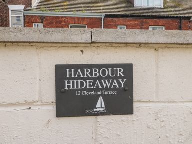 A sign on a white wall reading Harbour Hideaway 12 Cleveland Terrace with a sailboat icon in Whitby