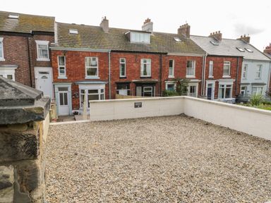 A gravel courtyard with low white walls and terraced red brick houses in the background at Harbour Hideaway Whitby