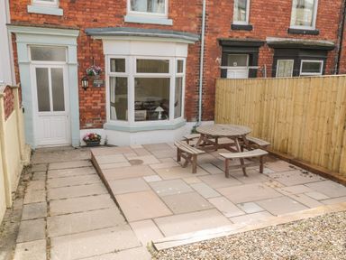 A patio area with a round wooden table and benches outside a red brick house at Harbour Hideaway in Whitby