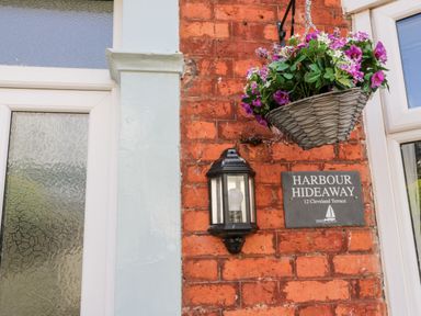A hanging basket with flowers next to a lantern and a sign on a brick wall at Harbour Hideaway Whitby
