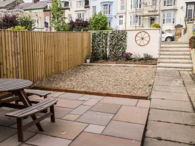 A backyard with a wooden picnic table gravel area flower bed stairs and wooden fence at Harbour Hideaway in Whitby