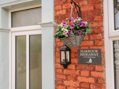 A hanging basket of flowers beside a light and a sign on a brick wall at Harbour Hideaway in Whitby