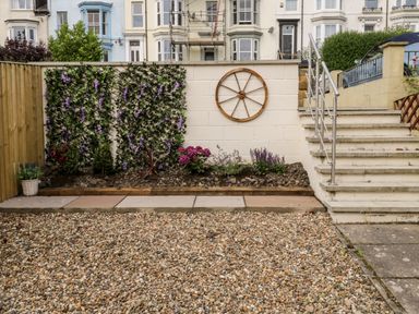 A backyard garden with gravel pathway flowers on a bed and a wooden wheel decoration on a wall at Harbour Hideaway in Whitby
