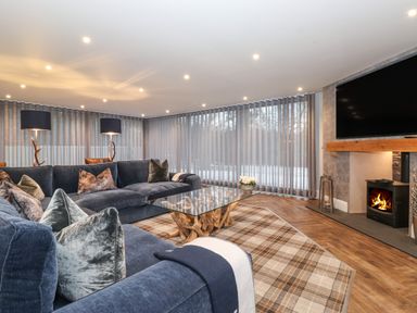 A living room with large blue sofas a glass coffee table with a wooden base plaid carpet floor lamps and a fireplace at Hares Breath in Bowness-On-Windermere