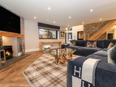 A living room with a sectional sofa a glass coffee table a fireplace and a wooden staircase at Hares Breath in Bowness-On-Windermere