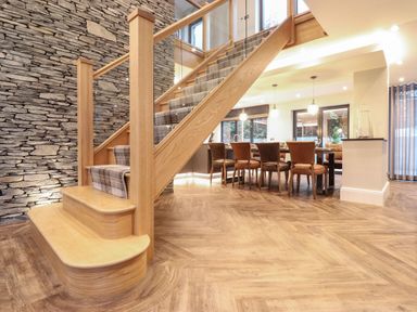 A wooden staircase with a carpet runner next to a dining table with chairs in a room with stone and plaster walls at Hares Breath in Bowness-On-Windermere