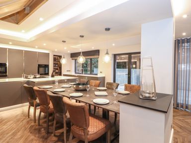 A dining area with a large table set with plates and glasses surrounded by chairs in a kitchen at Hares Breath in Bowness-On-Windermere