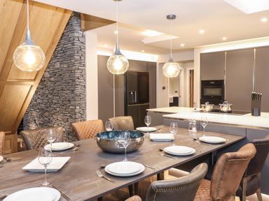 A dining table set with plates and glasses in a kitchen with stone wall and modern cabinets at Hares Breath in Bowness-On-Windermere