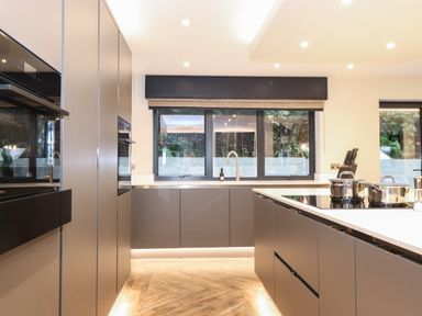 A modern kitchen with built-in ovens stainless steel pots on a countertop and large windows at Hares Breath in Bowness-On-Windermere