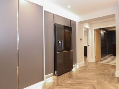 A hallway with built in cabinets and a black refrigerator with wooden floors at Hares Breath in Bowness-On-Windermere