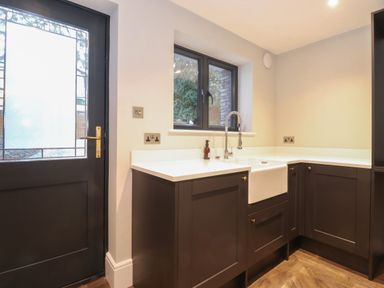 A kitchen corner with dark cabinets a white countertop a farmhouse sink and a window at Hares Breath in Bowness-On-Windermere