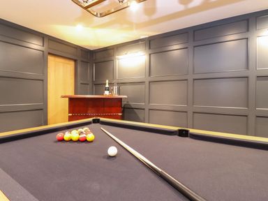 A pool table with balls and a cue stick in a room with dark paneled walls and a wooden door
