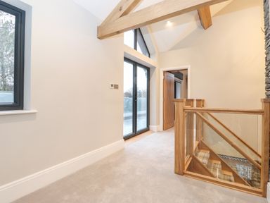 A landing area with wooden staircase railing glass panels a door window and sliding glass doors at Hares Breath in Bowness-On-Windermere