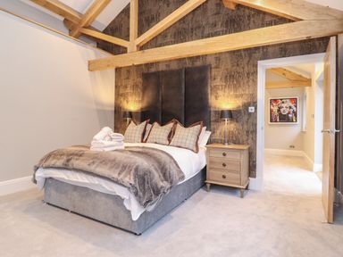 A bedroom with a bed, nightstand with lamps, and exposed wooden beams at Hare's Breath in Bowness-On-Windermere