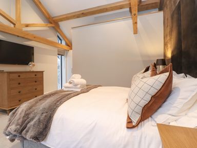 A bedroom with a bed with pillows and folded towels a wooden dresser and a wall mounted tv at Hares Breath in Bowness-On-Windermere