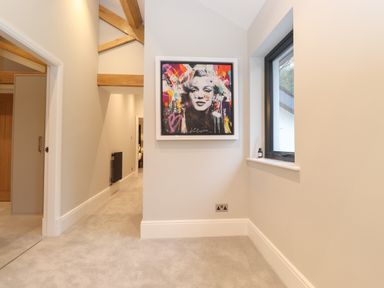 A hallway with a colorful framed artwork on the wall and a window with a small bottle on the sill at Hares Breath in Bowness-On-Windermere