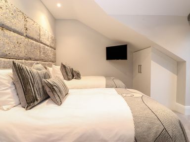 A bedroom with two beds grey pillows a mounted television and a built in wardrobe at Hares Breath in Bowness-On-Windermere