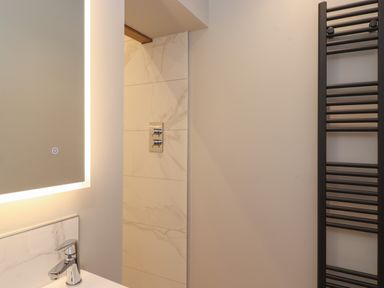 A bathroom with illuminated mirror a sink with faucet marble wall tiles and a black heated towel rail at Hares Breath in Bowness-On-Windermere