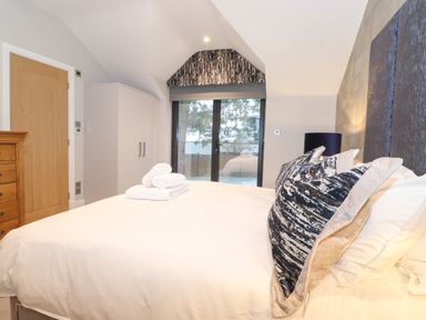 A bedroom with a double bed pillows folded towels wardrobe wooden chest of drawers and glass doors at Hares Breath in Bowness-On-Windermere