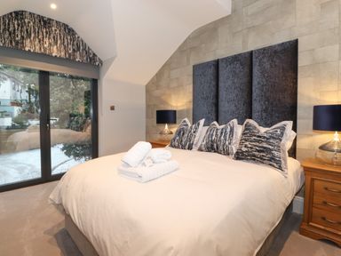 A bedroom with a bed pillows lamps on wooden bedside tables and glass doors at Hares Breath in Bowness-On-Windermere