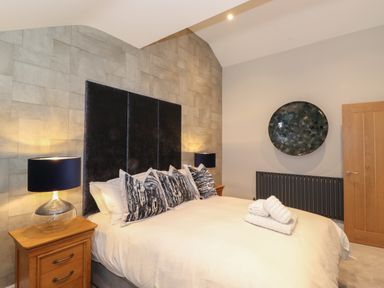 A bedroom with a large bed and wooden nightstands with lamps at Hares Breath in Bowness-On-Windermere