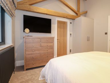 A bedroom with a wooden dresser and a wall mounted TV with exposed wooden ceiling beams at Hares Breath in Bowness-On-Windermere