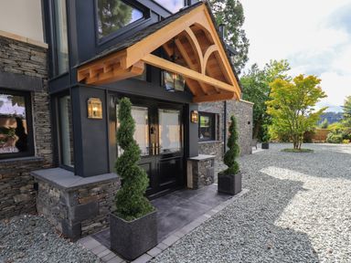The front entrance of a house with double black doors stone walls wooden porch and spiral topiary plants in pots at Hares Breath in Bowness-On-Windermere