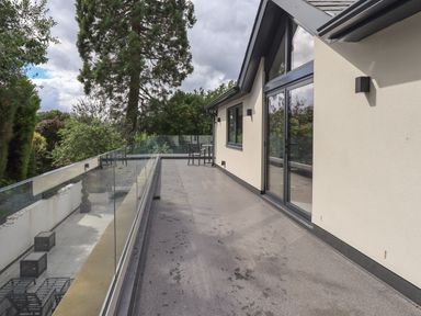 A balcony with glass railing and chairs outside a house surrounded by trees at Hares Breath in Bowness On Windermere