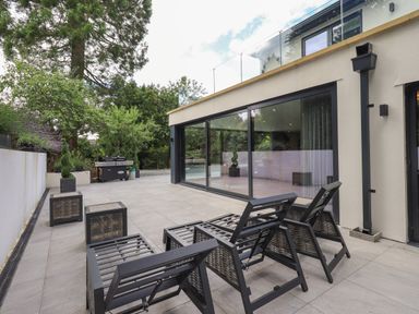 An outdoor patio with three black lounge chairs two side tables a grill and glass sliding doors at Hares Breath in Bowness-On-Windermere