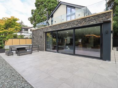 A patio with outdoor furniture and large sliding glass doors on a modern house at Hares Breath in Bowness-On-Windermere