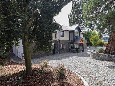 A modern two-story house with stone and white walls surrounded by gravel driveway and trees at Hare's Breath in Bowness-On-Windermere