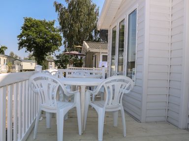 An outdoor deck with white plastic table and chairs attached to a mobile home at The Goodwood Lodge in Runcton near Chichester