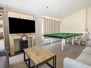 A living room with a television above a fireplace, a clock, a pool table, and chairs at The Goodwood Lodge in Runcton near Chichester