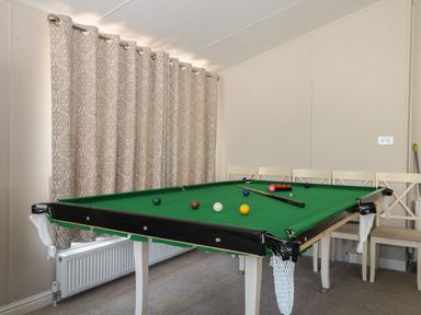 A room with a pool table with balls and cue sticks and chairs along the wall with patterned curtains and a radiator at The Goodwood Lodge in Runcton near Chichester