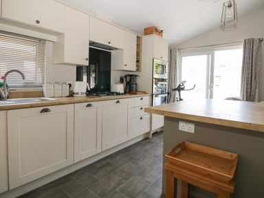 A kitchen with white cabinets wooden countertops dishwasher kettle toaster coffee maker and exercise bike by sliding glass doors at The Goodwood Lodge in Runcton near Chichester