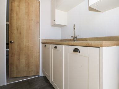 A kitchen area with cream cabinets wooden countertop and a stainless steel faucet at The Goodwood Lodge in Runcton near Chichester