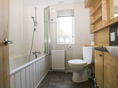 A bathroom with bathtub shower toilet window and wooden cabinets at The Goodwood Lodge in Runcton near Chichester